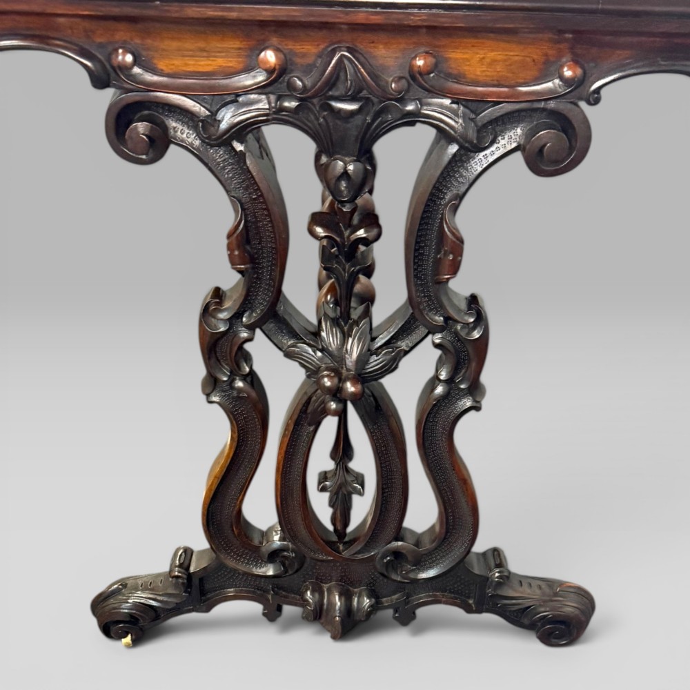 An Early Victorian rectangular centre table featuring a figured zebrawood veneered top, carved aprons, and carved rosewood trestle standards with scrolled feet. View VII