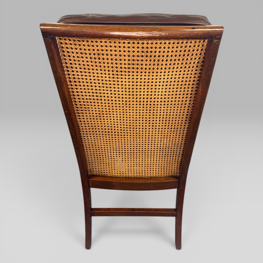 A Regency mahogany bergere armchair featuring dark brown leather cushions, woven cane side panels, scroll arms, and reeded front legs with brass castors. View VII
