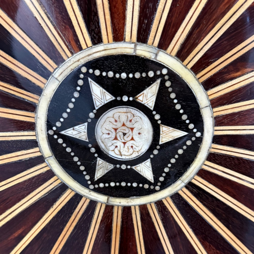 Overhead view of a circular centre table top showing radiating calamander wood veneers, light stringing, a central star motif, and a carved ebony border. View V
