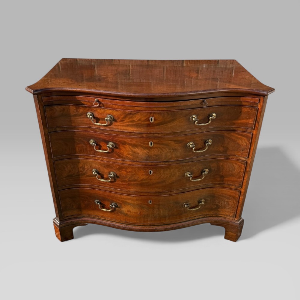 An 18th-century Georgian mahogany chest of drawers featuring a curved serpentine front, four graduated drawers, brass swan-neck handles, and a pull-out brushing slide.