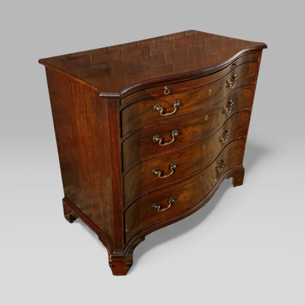 An 18th-century Georgian mahogany chest of drawers featuring a curved serpentine front, four graduated drawers, brass swan-neck handles, and a pull-out brushing slide. View II