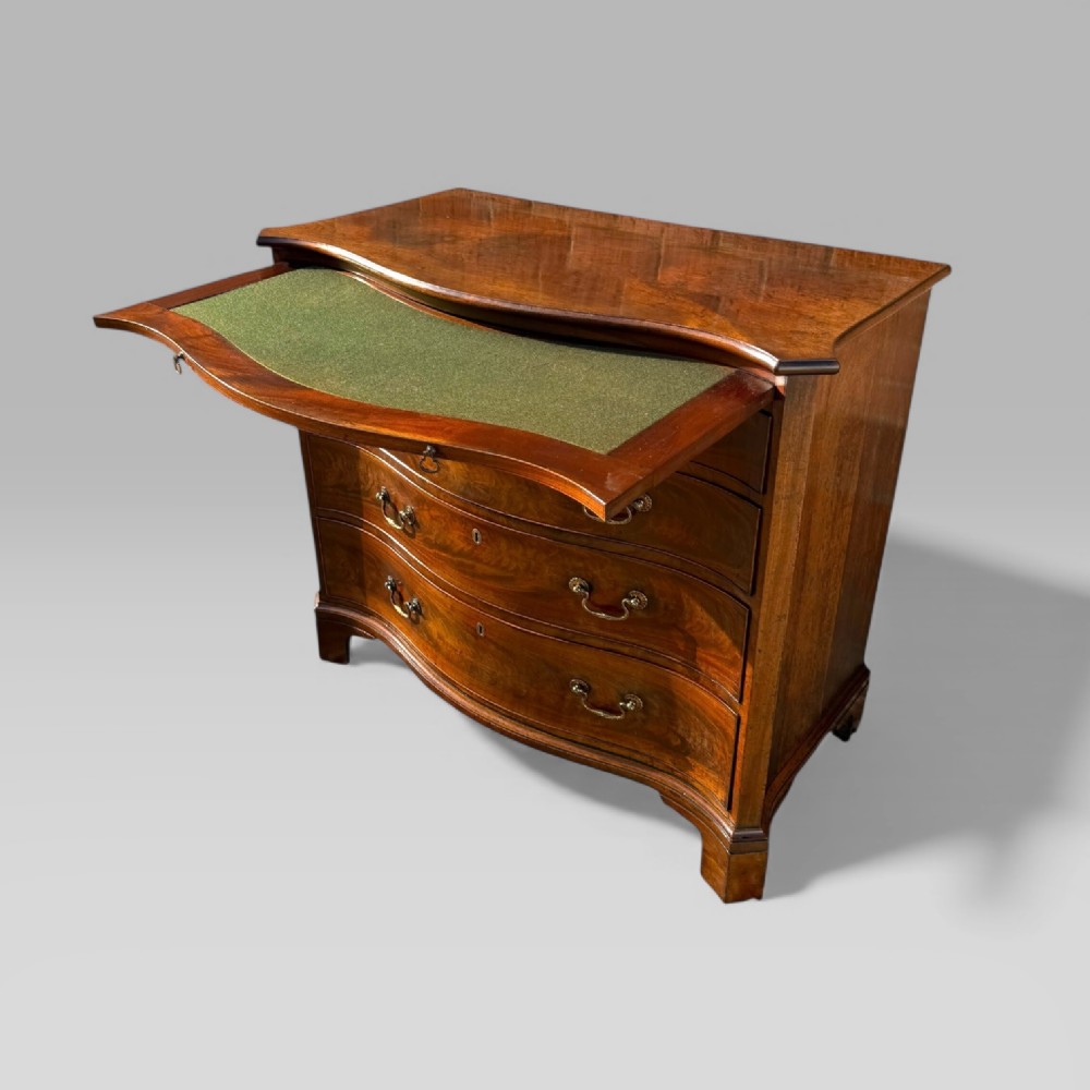 An 18th-century Georgian mahogany chest of drawers featuring a curved serpentine front, four graduated drawers, brass swan-neck handles, and a pull-out brushing slide. View VIII