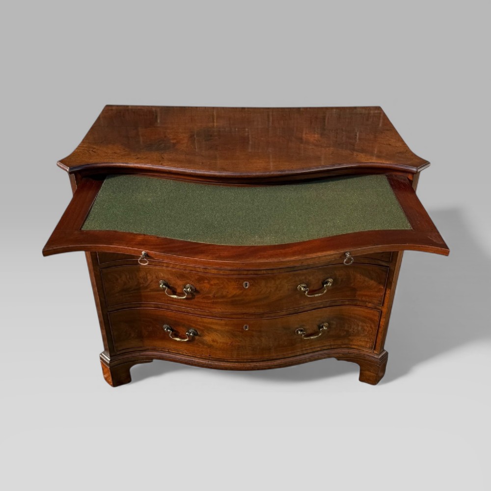 An 18th-century Georgian mahogany chest of drawers featuring a curved serpentine front, four graduated drawers, brass swan-neck handles, and a pull-out brushing slide. View IX
