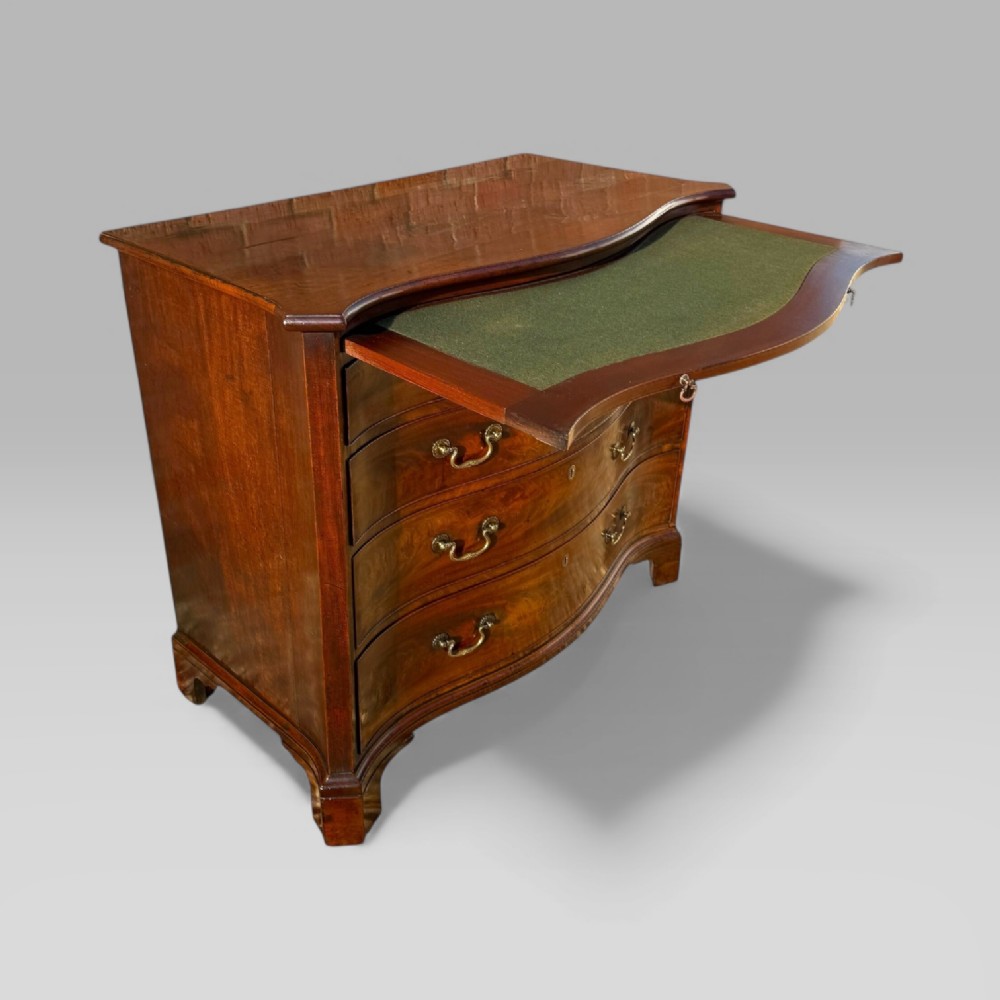 An 18th-century Georgian mahogany chest of drawers featuring a curved serpentine front, four graduated drawers, brass swan-neck handles, and a pull-out brushing slide. View X