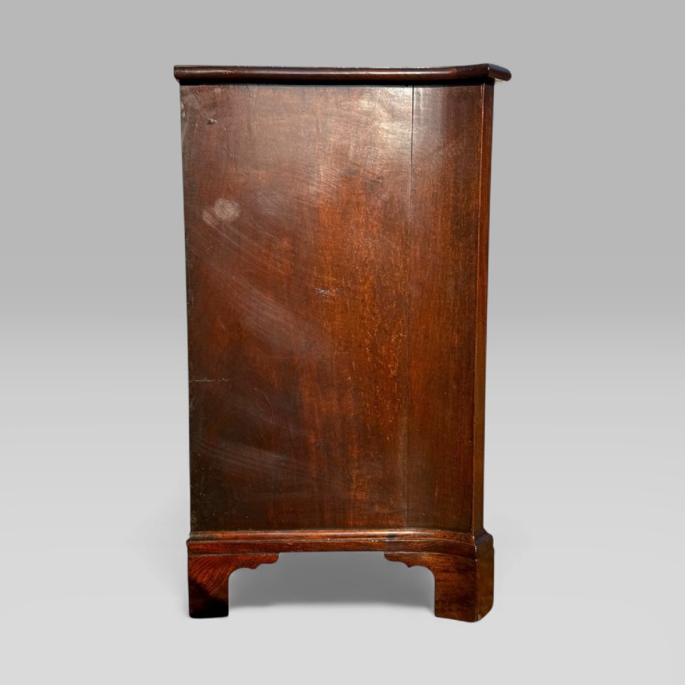 An 18th-century Georgian mahogany chest of drawers featuring a curved serpentine front, four graduated drawers, brass swan-neck handles, and a pull-out brushing slide. View XII