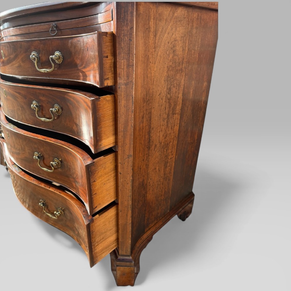 An 18th-century Georgian mahogany chest of drawers featuring a curved serpentine front, four graduated drawers, brass swan-neck handles, and a pull-out brushing slide. View XIII