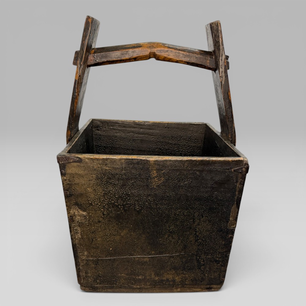 An antique dark brown Chinese elm harvest bucket featuring a tapered square body and a high wooden carrying handle with mortise and tenon joinery. View II