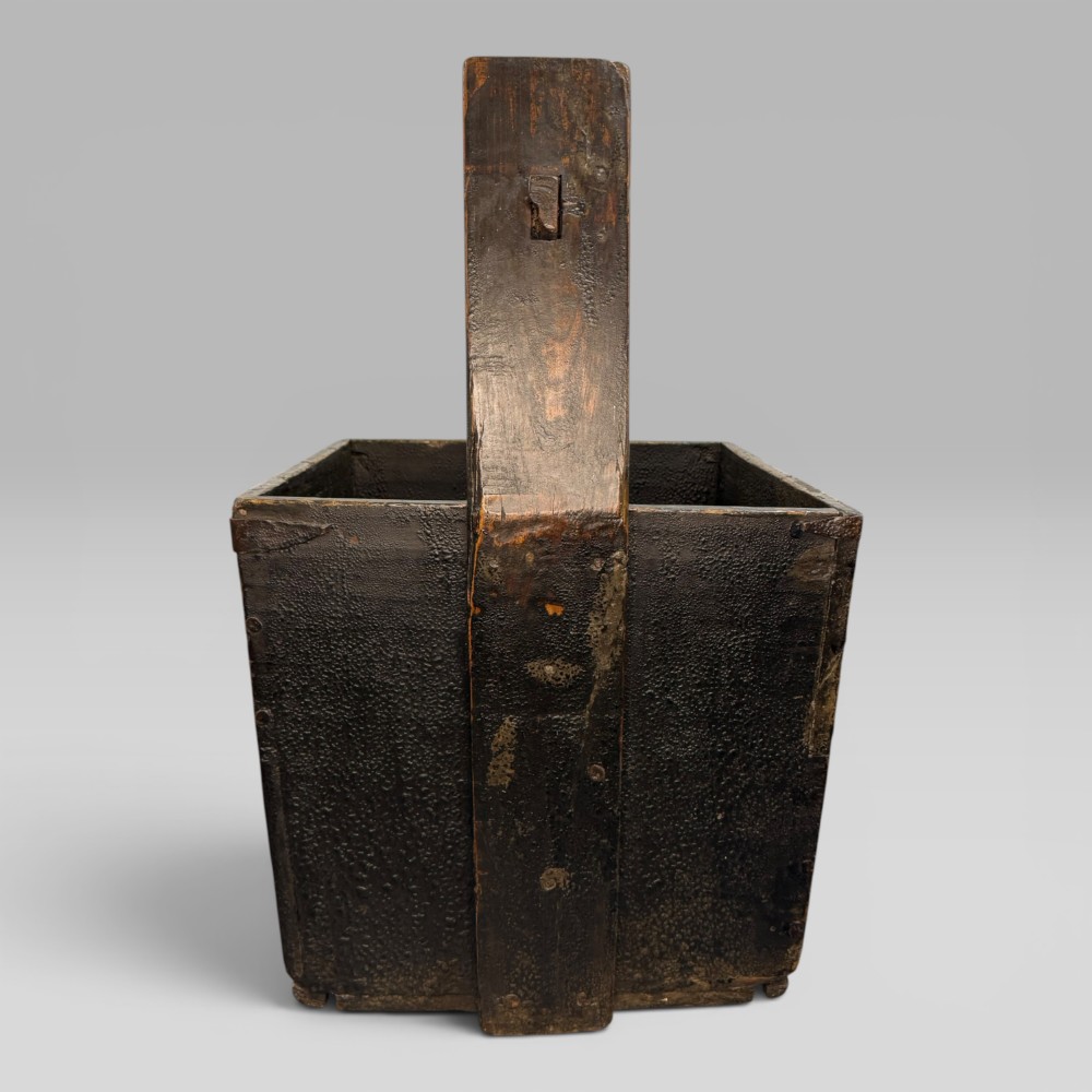 An antique dark brown Chinese elm harvest bucket featuring a tapered square body and a high wooden carrying handle with mortise and tenon joinery. View IV