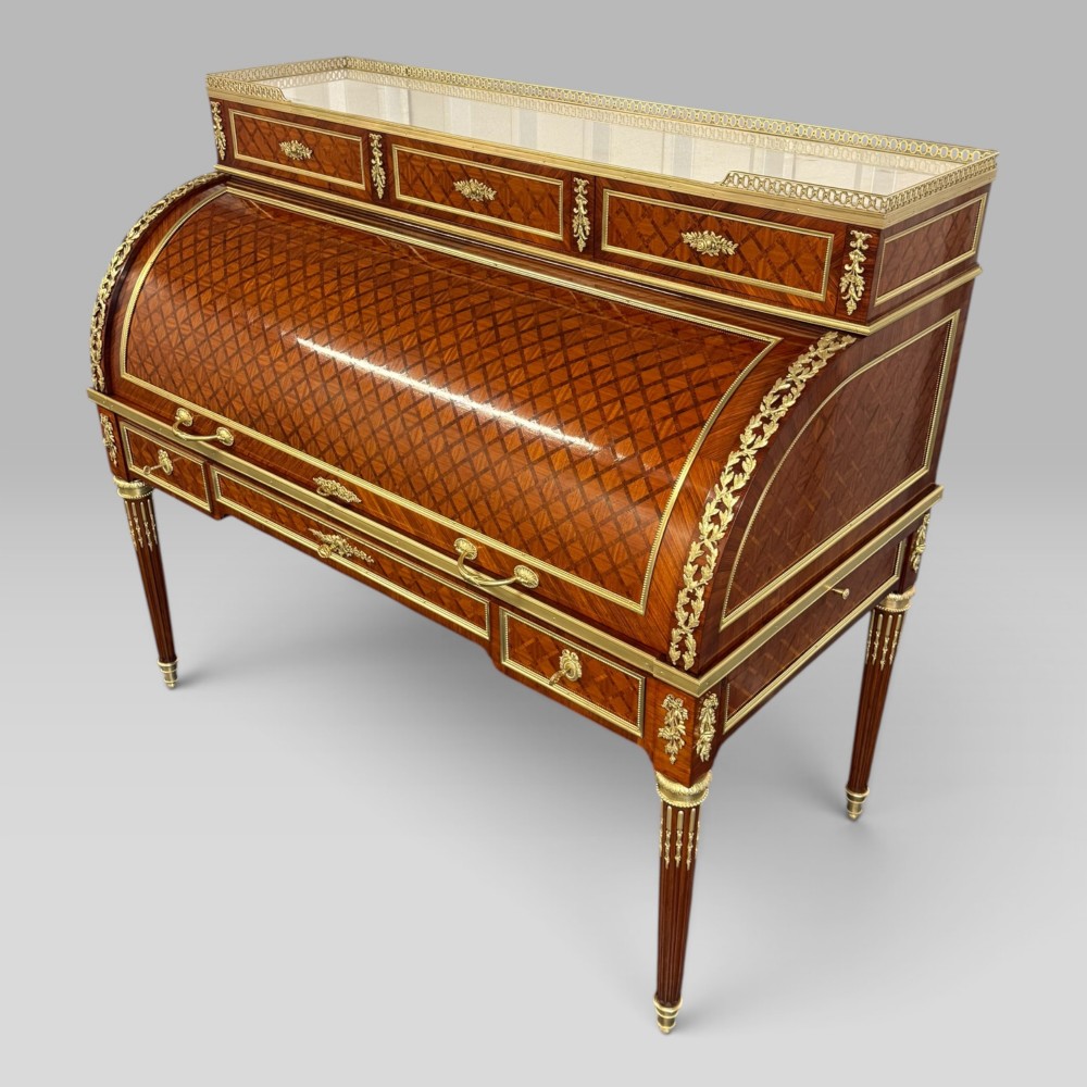 A French Louis XVI style cylinder desk featuring detailed geometric diamond parquetry, gilded bronze mounts, a top brass gallery rail, and slender fluted legs.
