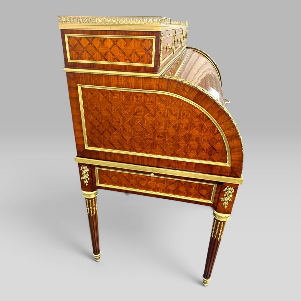 A French Louis XVI style cylinder desk featuring detailed geometric diamond parquetry, gilded bronze mounts, a top brass gallery rail, and slender fluted legs. View XI