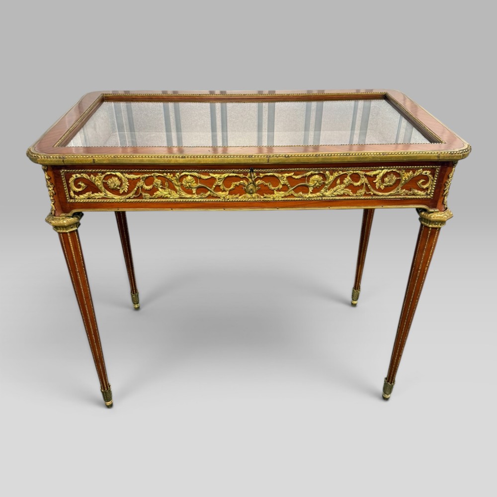 A rectangular French Louis XVI style bijouterie display table featuring a glazed glass top, decorative gilt bronze mounts along the frieze, and slender tapered legs ending in brass sabots. View II