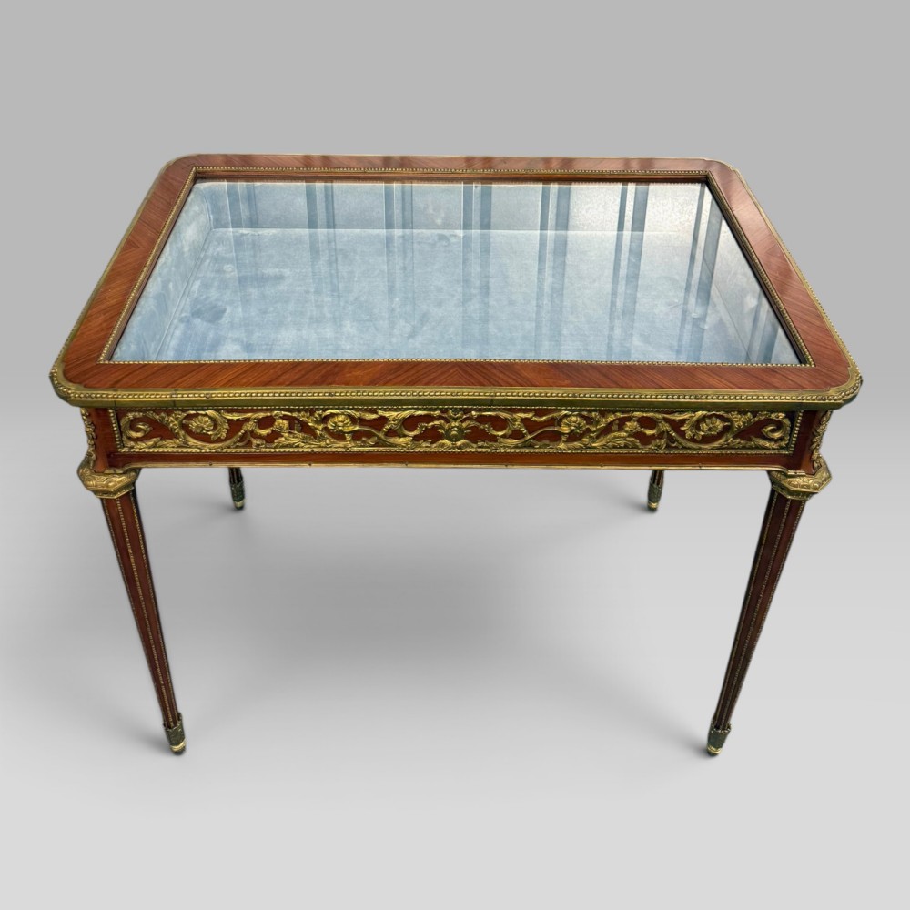 A rectangular French Louis XVI style bijouterie display table featuring a glazed glass top, decorative gilt bronze mounts along the frieze, and slender tapered legs ending in brass sabots. View III