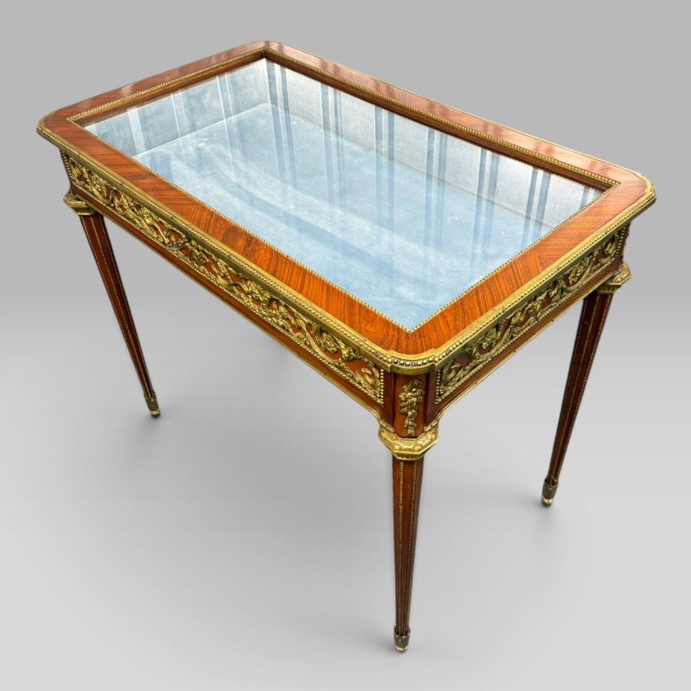 A rectangular French Louis XVI style bijouterie display table featuring a glazed glass top, decorative gilt bronze mounts along the frieze, and slender tapered legs ending in brass sabots. View IV