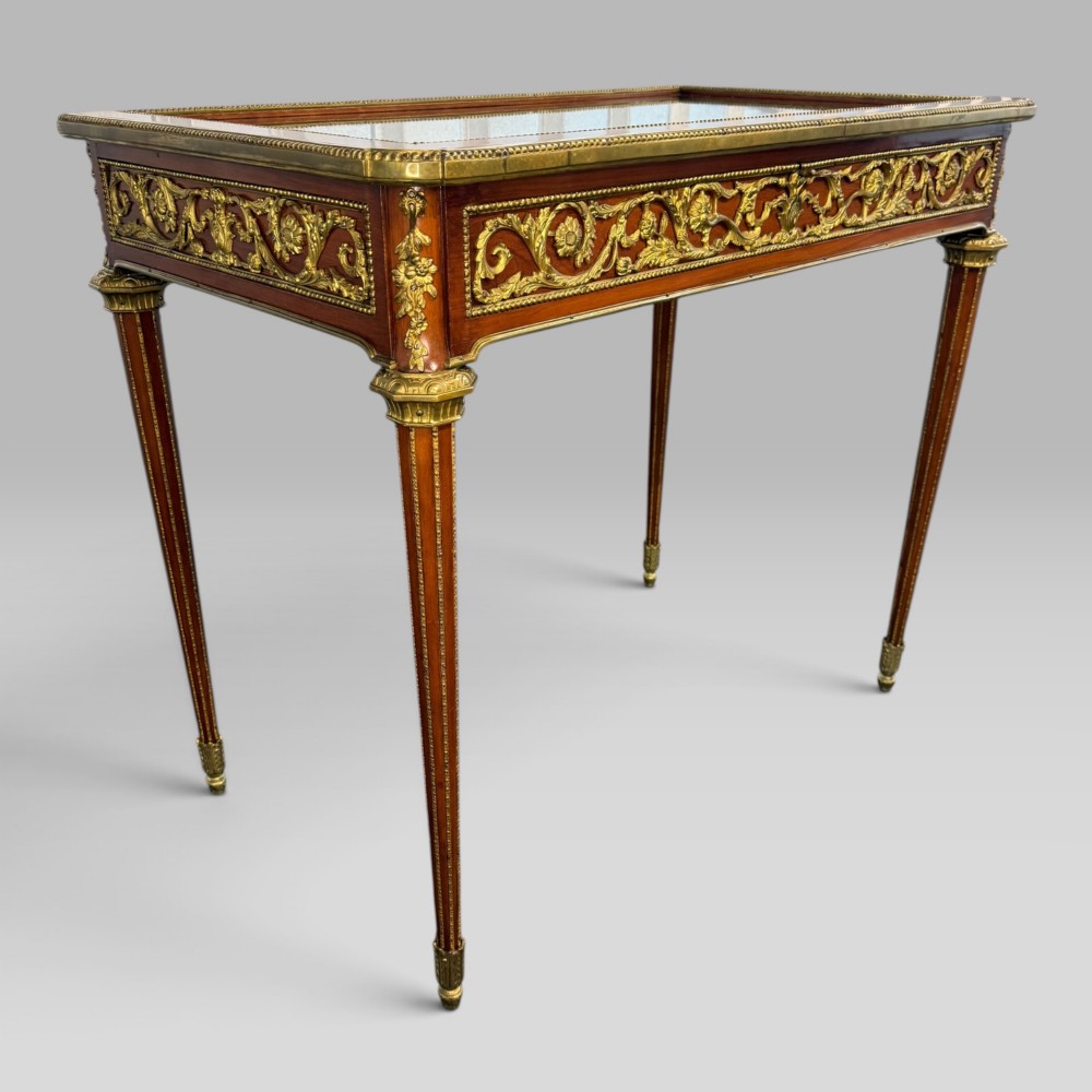 A rectangular French Louis XVI style bijouterie display table featuring a glazed glass top, decorative gilt bronze mounts along the frieze, and slender tapered legs ending in brass sabots. View IX