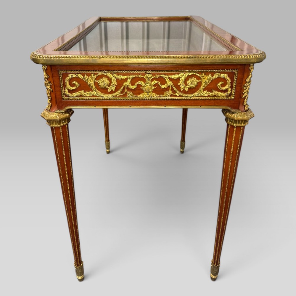 A rectangular French Louis XVI style bijouterie display table featuring a glazed glass top, decorative gilt bronze mounts along the frieze, and slender tapered legs ending in brass sabots. View XI