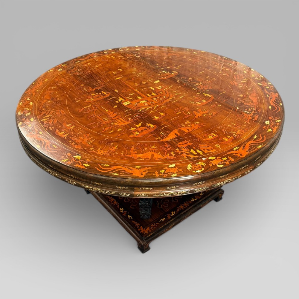 A circular dark rosewood centre table featuring detailed marquetry inlays depicting ships, pagodas, and flora.