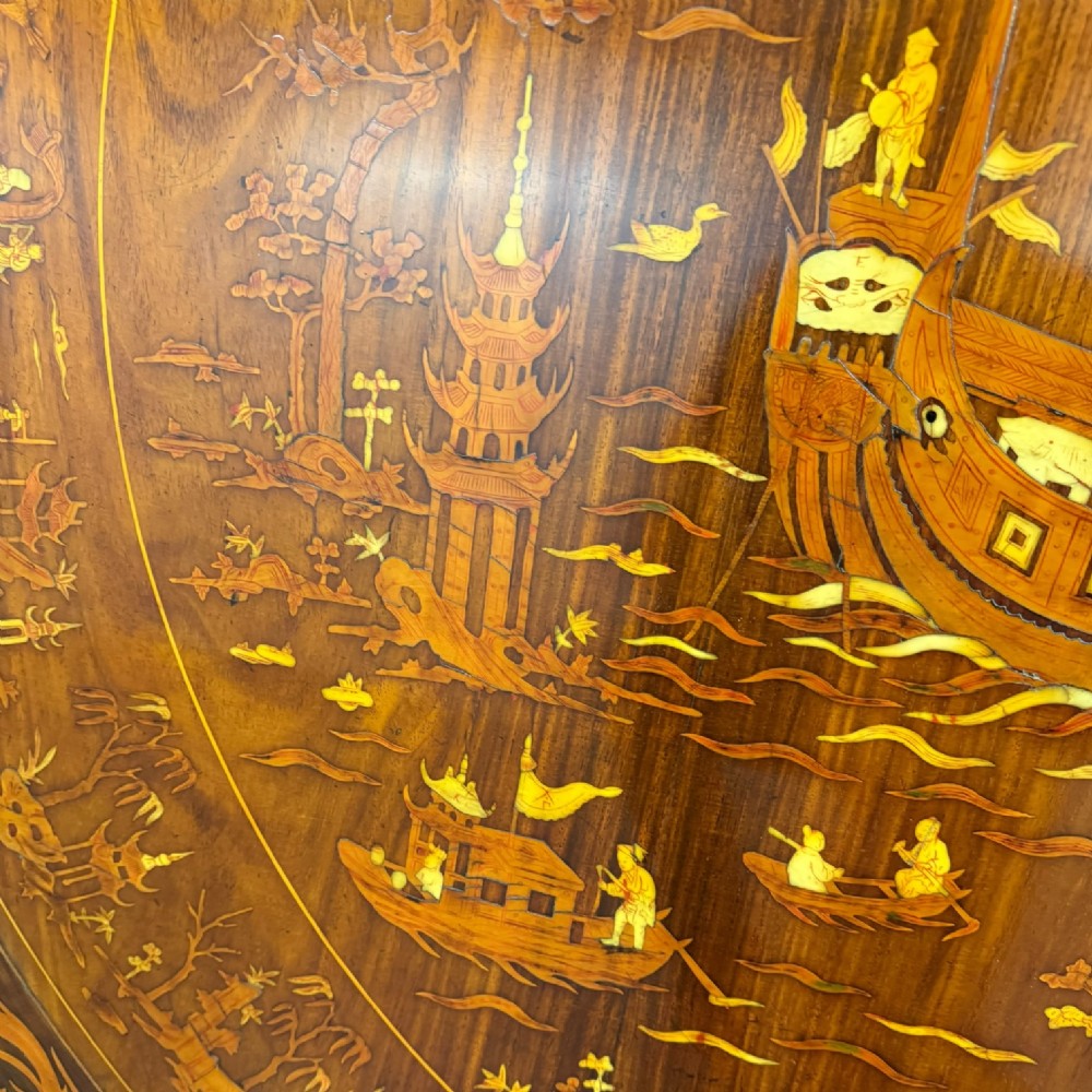 A circular dark rosewood centre table featuring detailed marquetry inlays depicting ships, pagodas, and flora. View XII