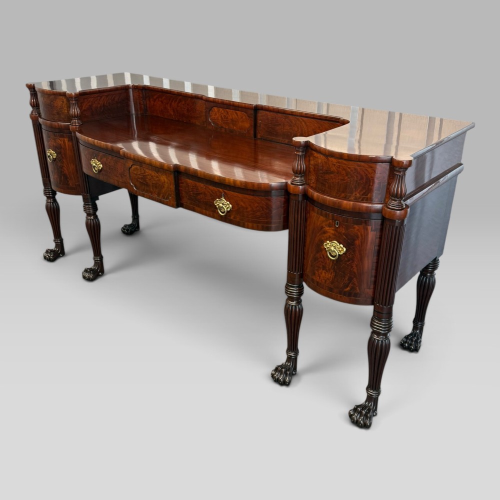 An antique Regency flame mahogany sideboard featuring a breakfront top, reeded columns, brass ring handles, and six carved lion paw feet.
