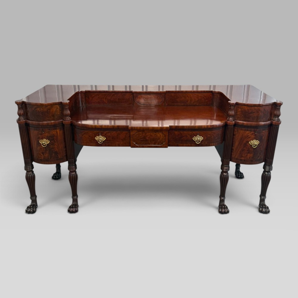 An antique Regency flame mahogany sideboard featuring a breakfront top, reeded columns, brass ring handles, and six carved lion paw feet. View II