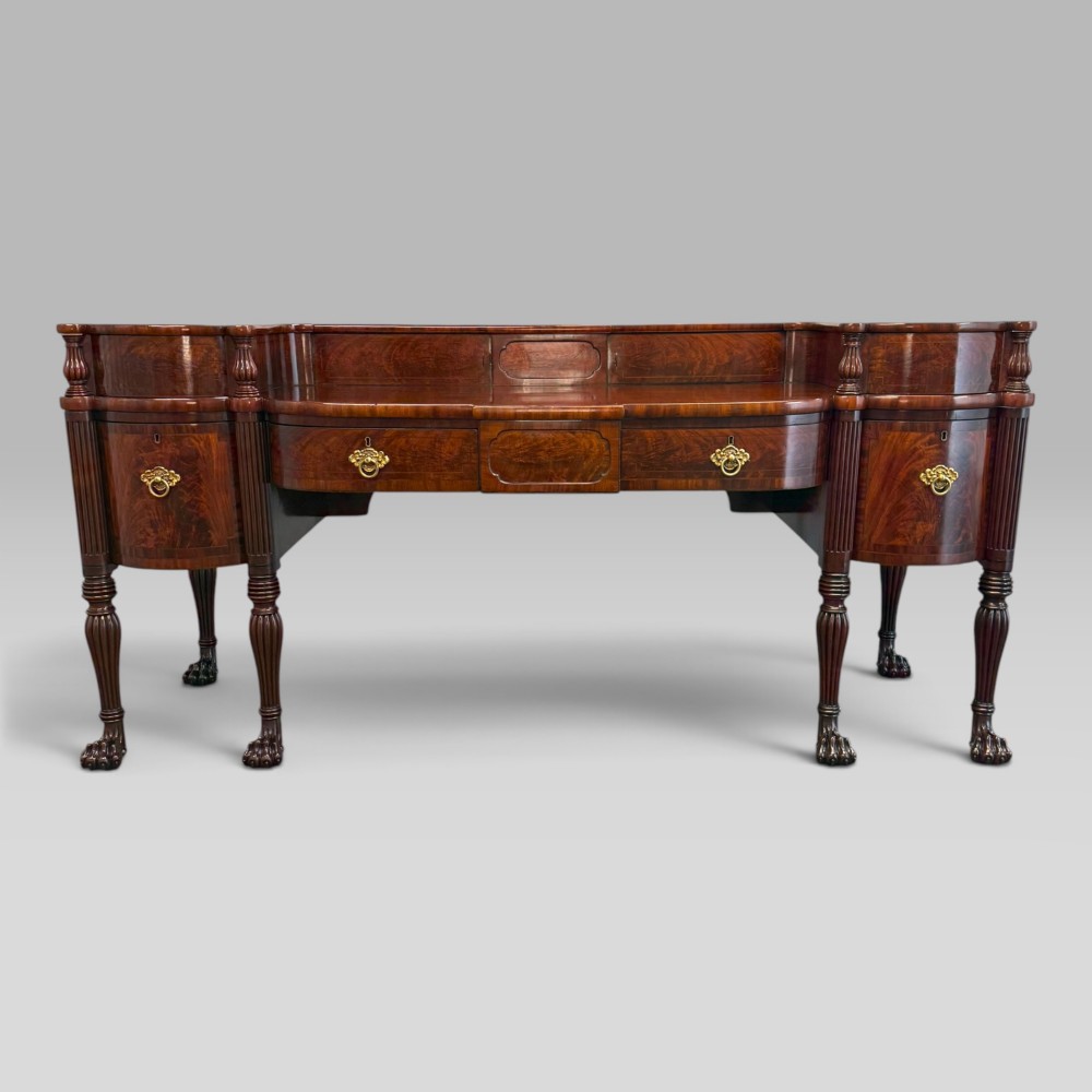 An antique Regency flame mahogany sideboard featuring a breakfront top, reeded columns, brass ring handles, and six carved lion paw feet. View IV