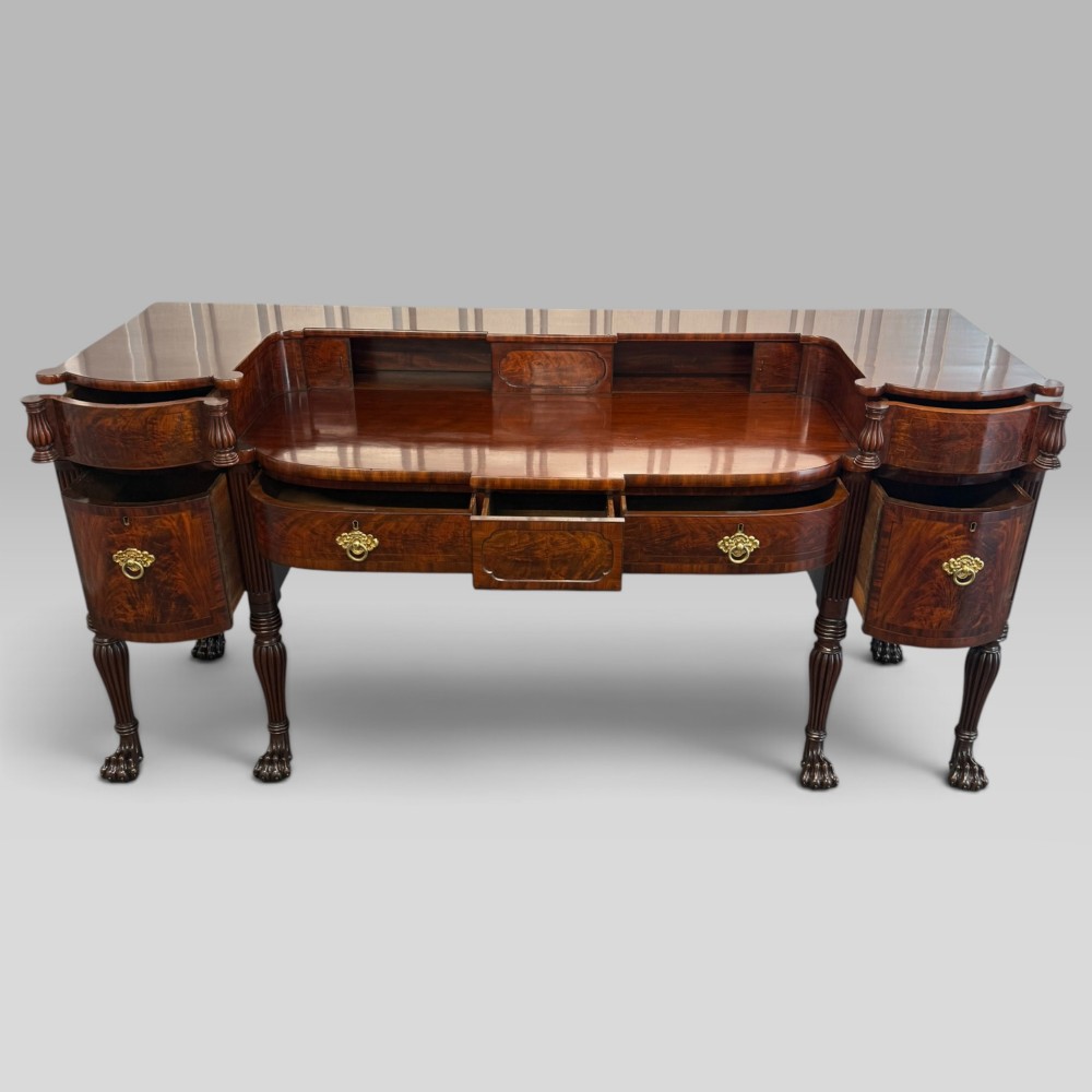 An antique Regency flame mahogany sideboard featuring a breakfront top, reeded columns, brass ring handles, and six carved lion paw feet. View V
