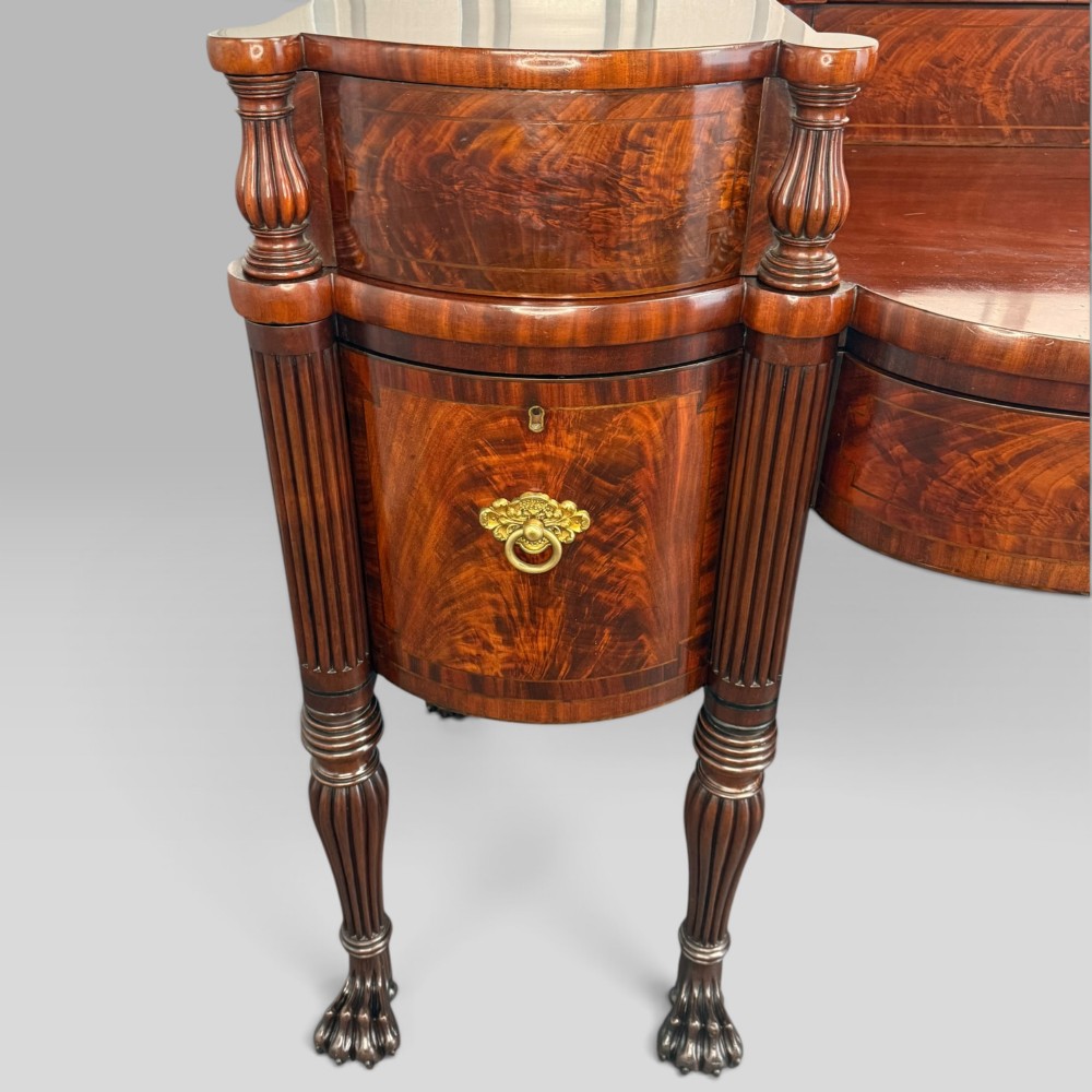 An antique Regency flame mahogany sideboard featuring a breakfront top, reeded columns, brass ring handles, and six carved lion paw feet. View VIII