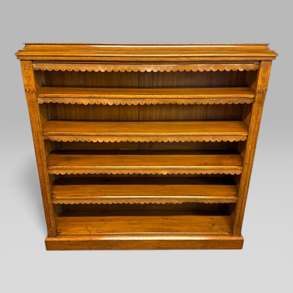 A late Victorian golden oak open bookcase featuring five open shelves decorated with scalloped edge trim and incised geometric carvings along the upright side panels. View II