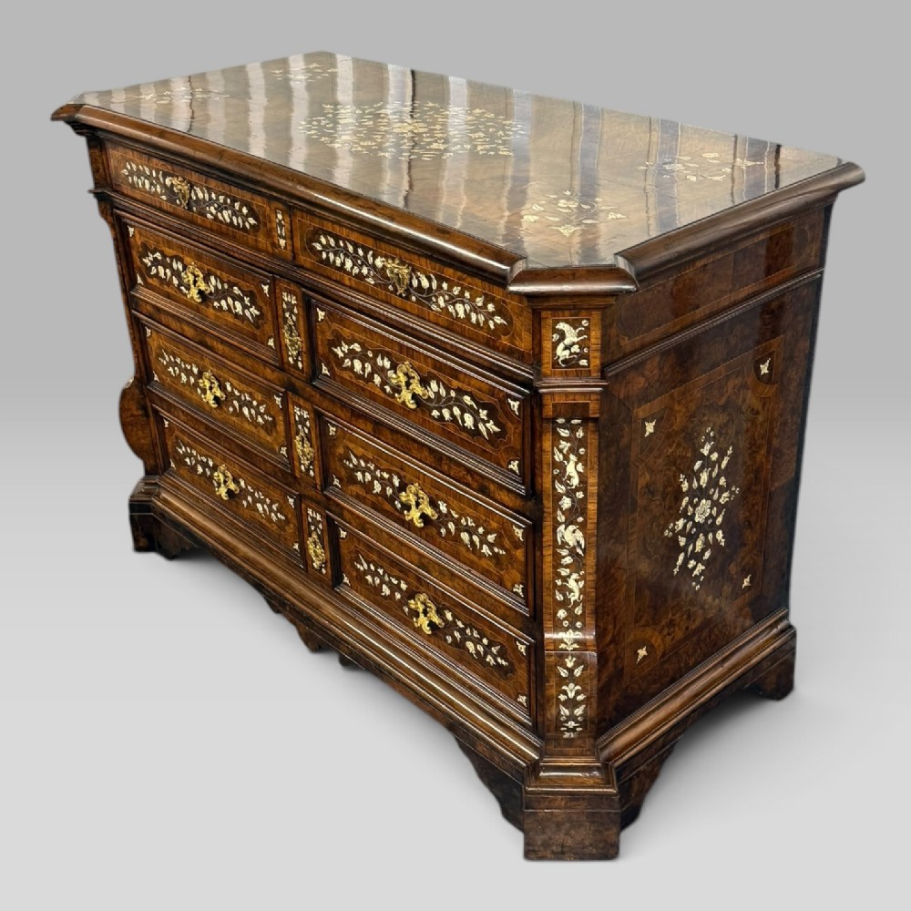 An Italian Baroque walnut commode featuring floral bone inlays across six drawer fronts, side panels, and top surface, supported by bracket feet.