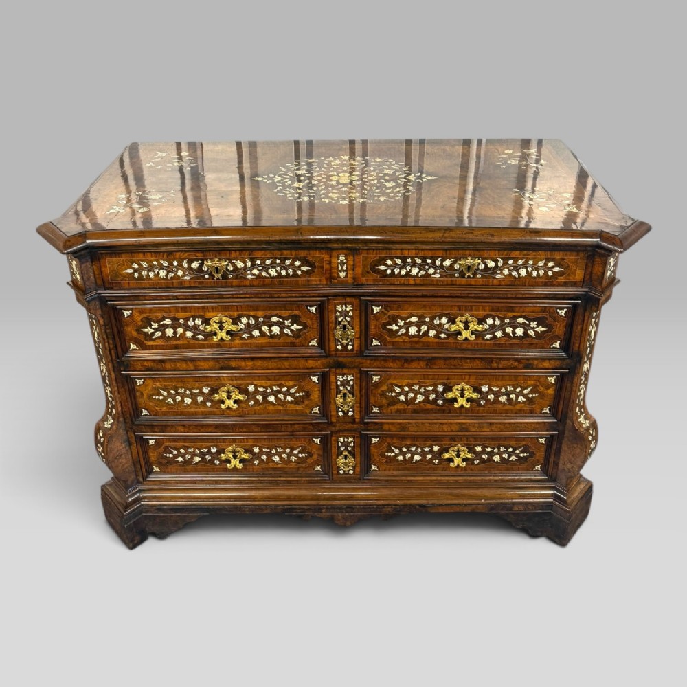 An Italian Baroque walnut commode featuring floral bone inlays across six drawer fronts, side panels, and top surface, supported by bracket feet. View II