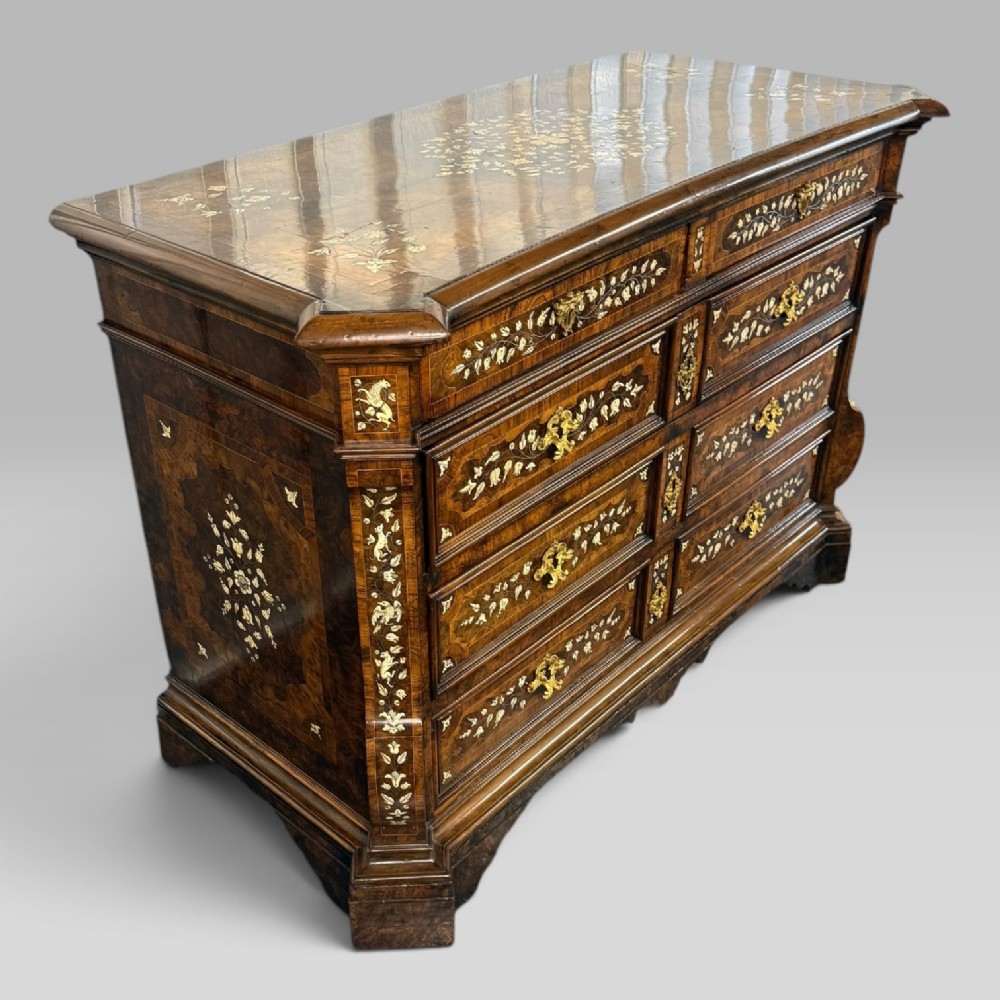 An Italian Baroque walnut commode featuring floral bone inlays across six drawer fronts, side panels, and top surface, supported by bracket feet. View III
