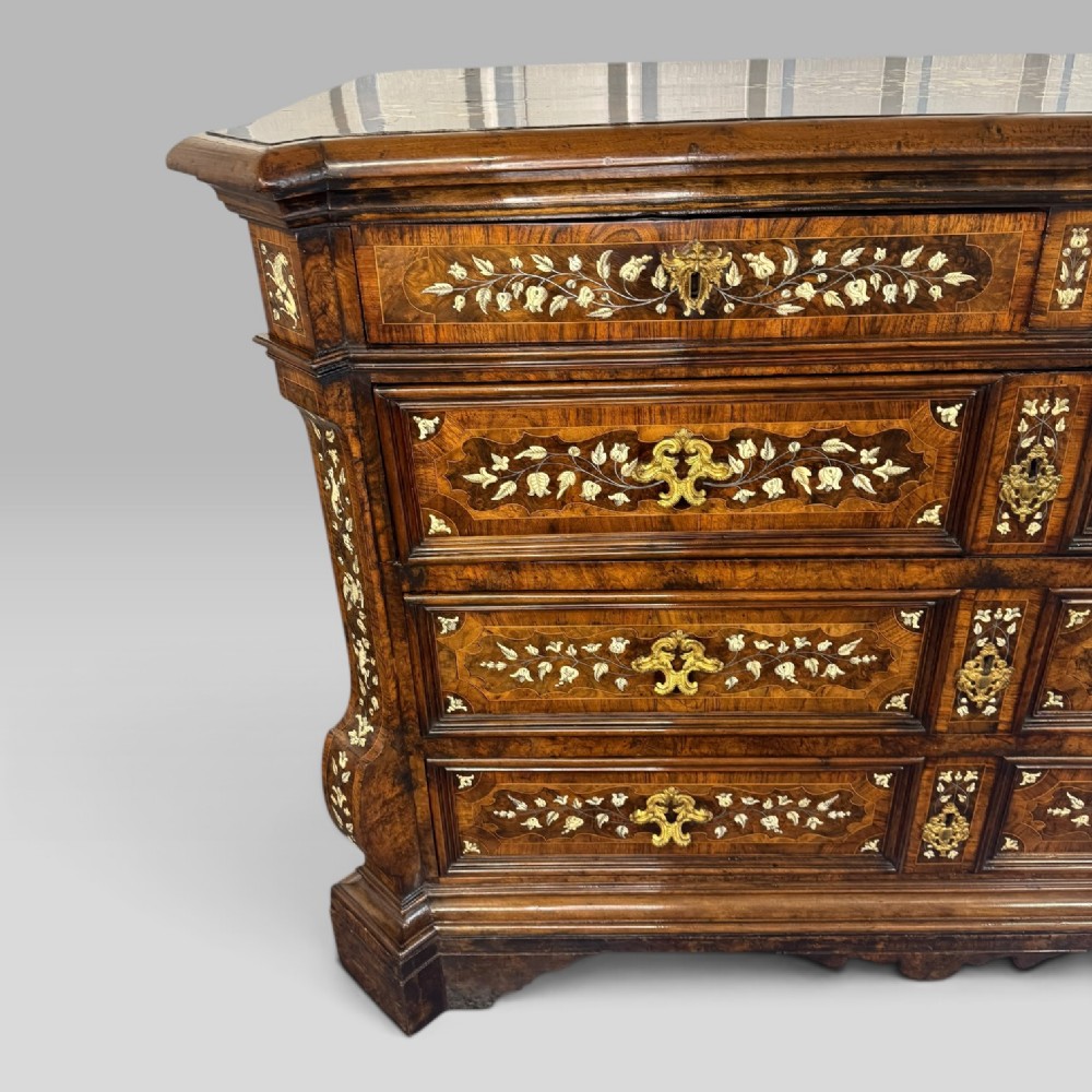 An Italian Baroque walnut commode featuring floral bone inlays across six drawer fronts, side panels, and top surface, supported by bracket feet. View IV