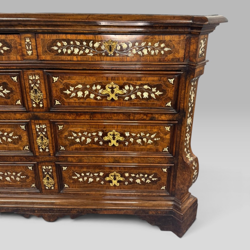 An Italian Baroque walnut commode featuring floral bone inlays across six drawer fronts, side panels, and top surface, supported by bracket feet. View V