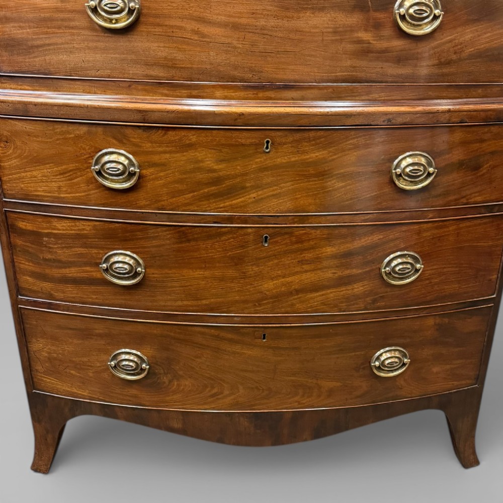 An antique Georgian bow-front mahogany chest on chest featuring a carved cornice, two upper short drawers, five long graduating drawers, and brass oval handles. View II