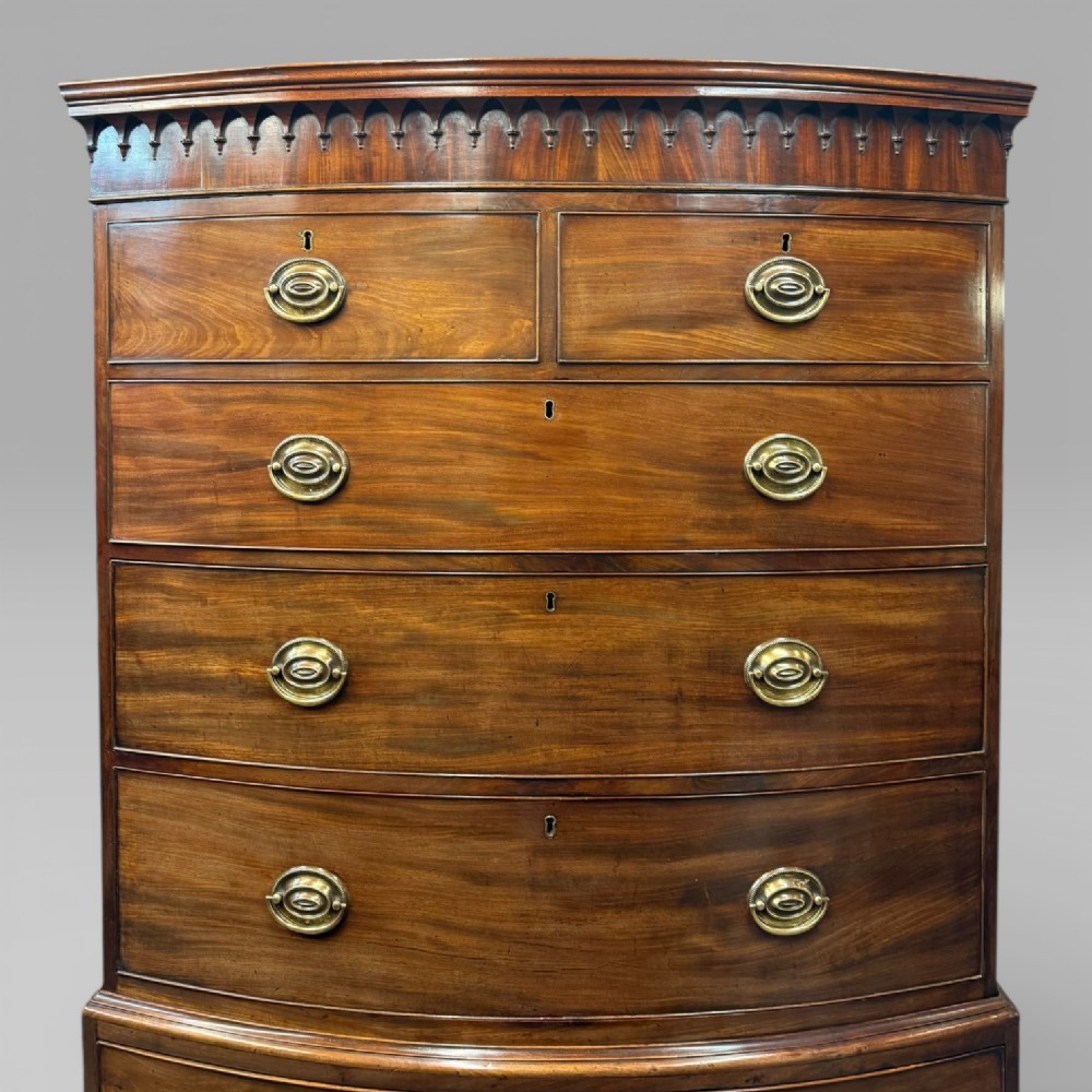 An antique Georgian bow-front mahogany chest on chest featuring a carved cornice, two upper short drawers, five long graduating drawers, and brass oval handles. View V
