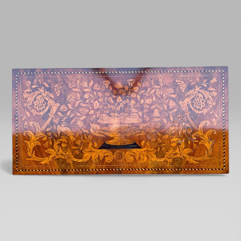 An antique Dutch mahogany console cabinet heavily decorated with intricate floral marquetry, featuring a single drawer above a rounded central cupboard door, flanked by turned columns. View V