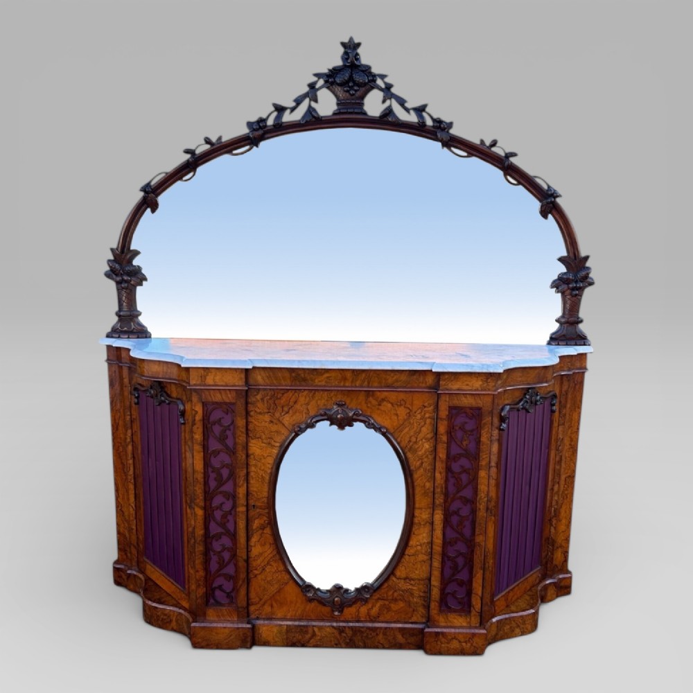 An antique Victorian burr walnut credenza featuring a white marble top, arched mirror back frame, central oval mirror door, and carved timber detailing.