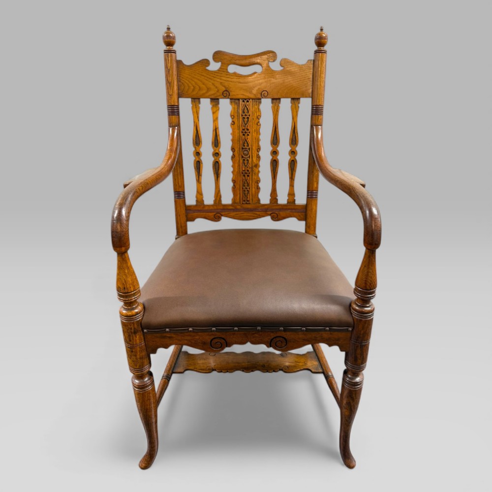 A Victorian golden oak armchair featuring a carved backrest, curved arms, brown leather seat with brass studs, and turned legs. View IV