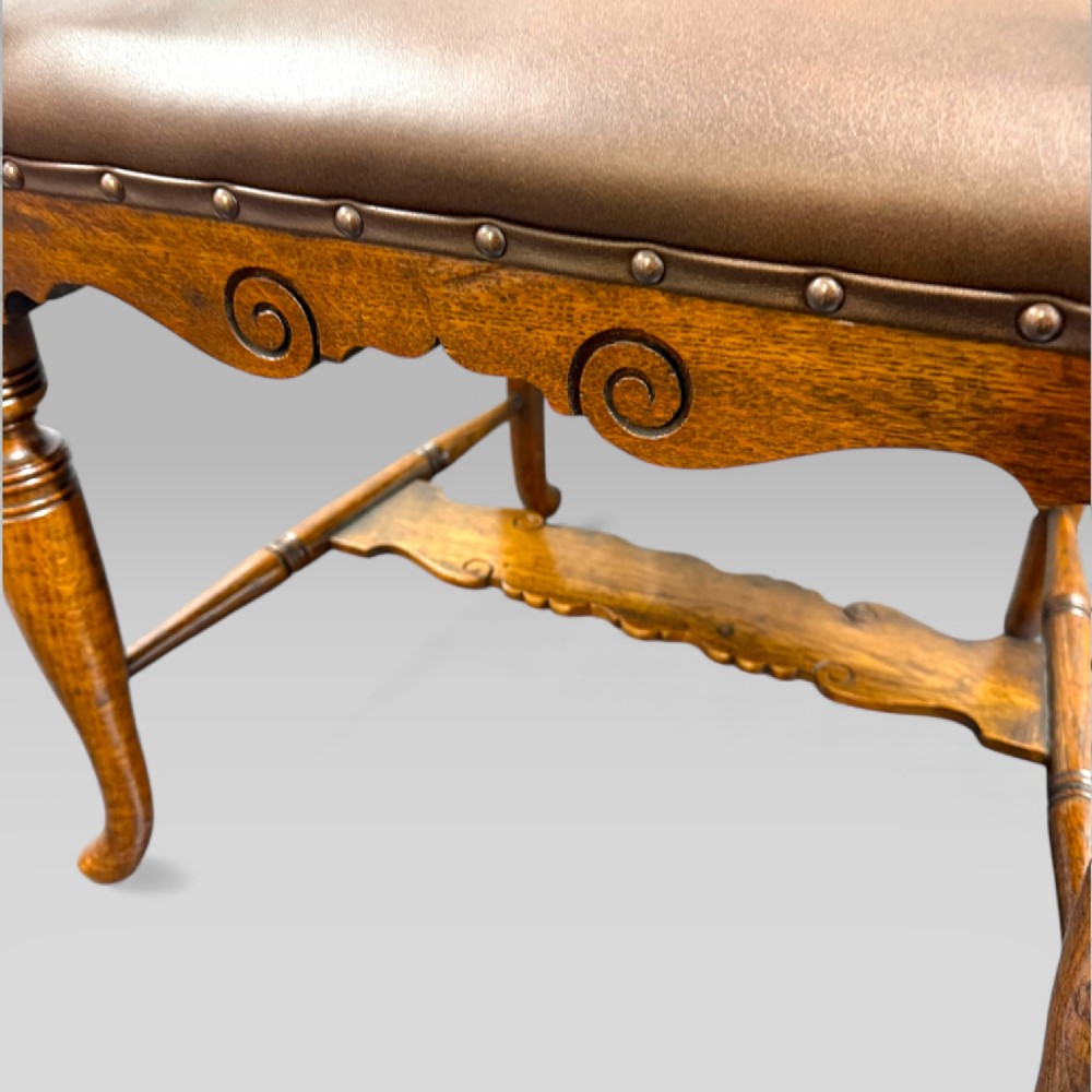 A Victorian golden oak armchair featuring a carved backrest, curved arms, brown leather seat with brass studs, and turned legs. View VIII
