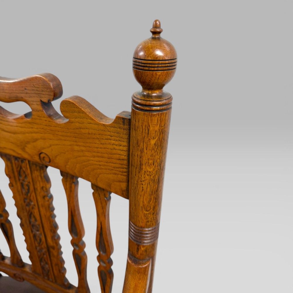 A Victorian golden oak armchair featuring a carved backrest, curved arms, brown leather seat with brass studs, and turned legs. View IX