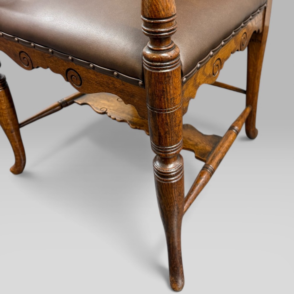 A Victorian golden oak armchair featuring a carved backrest, curved arms, brown leather seat with brass studs, and turned legs. View XII