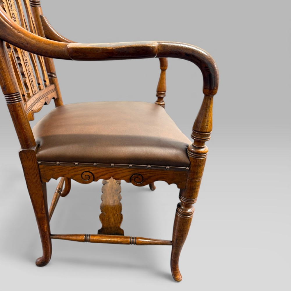 A Victorian golden oak armchair featuring a carved backrest, curved arms, brown leather seat with brass studs, and turned legs. View XIV