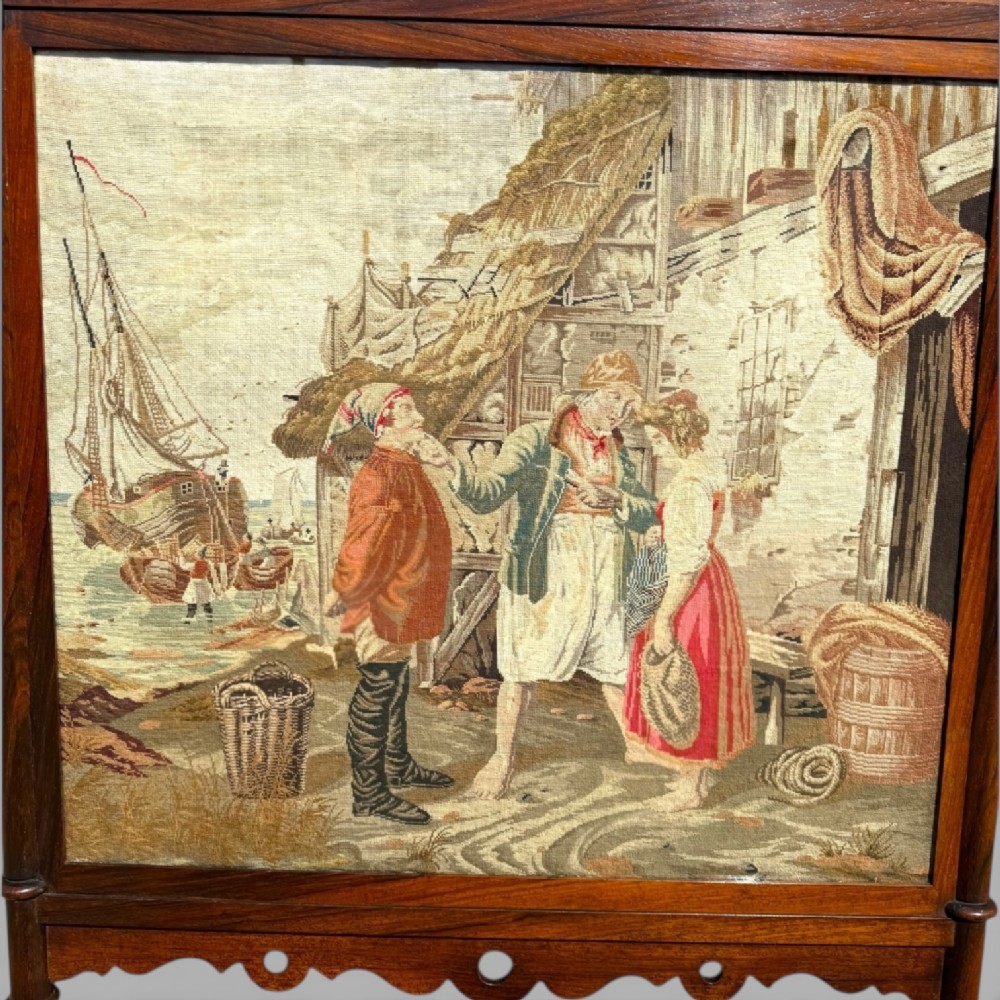 An antique Victorian dark rosewood cheval fire screen framing a needlepoint textile panel depicting figures by a coastal harbour. View VIII