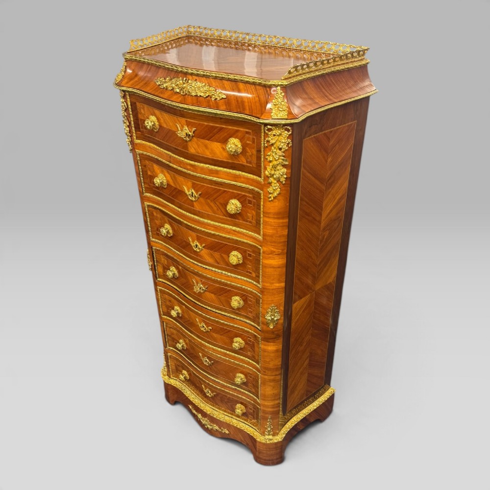 A tall antique French kingwood and rosewood secretaire chest featuring parquetry veneers, ornate gilt bronze mounts, seven drawer fronts, and a pierced brass gallery top.