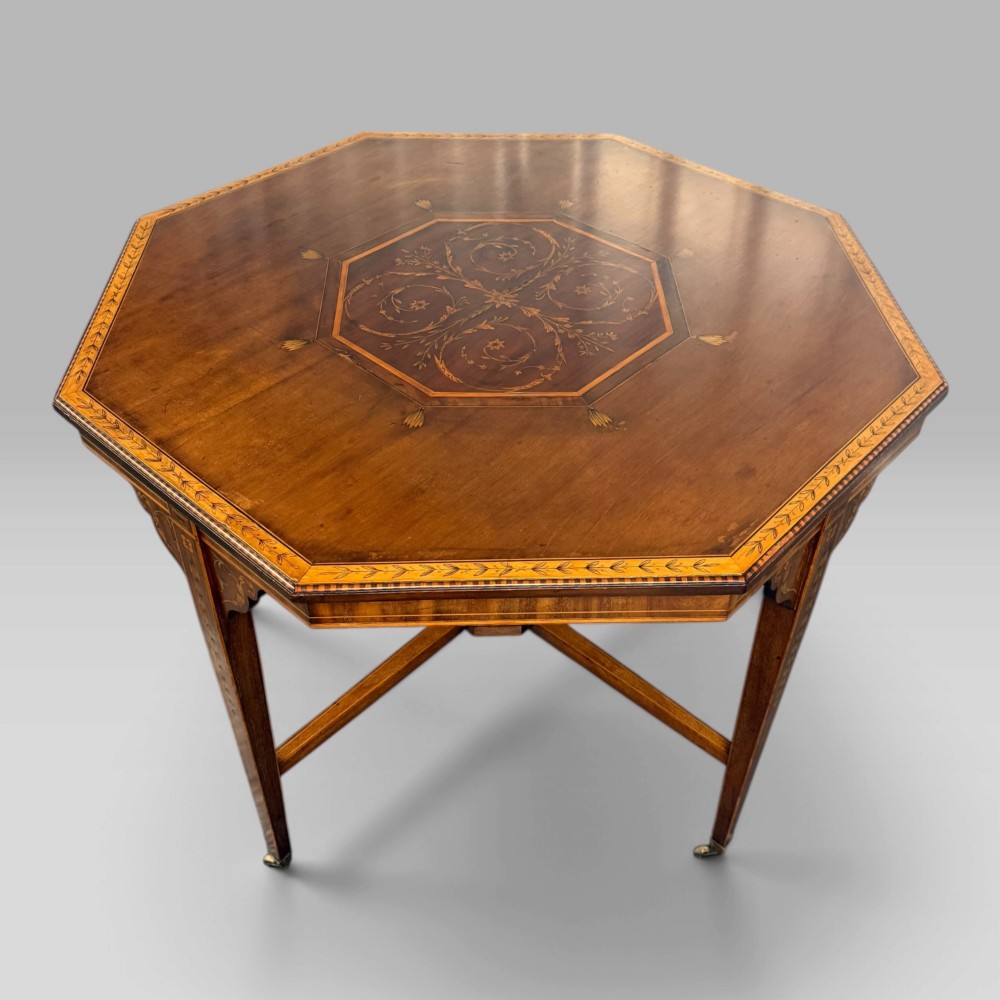 An octagonal Edwardian mahogany centre table featuring floral marquetry inlays, satinwood crossbanded borders, tapered legs, an X-stretcher, and brass castors. View III