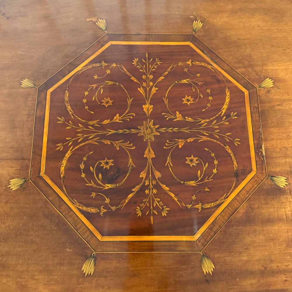 An octagonal Edwardian mahogany centre table featuring floral marquetry inlays, satinwood crossbanded borders, tapered legs, an X-stretcher, and brass castors. View VII