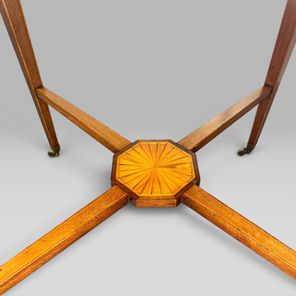 An octagonal Edwardian mahogany centre table featuring floral marquetry inlays, satinwood crossbanded borders, tapered legs, an X-stretcher, and brass castors. View VIII