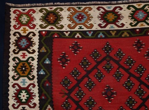 fig 1. A flatwoven antique Turkish Sarkoy kilim rug featuring a soft red central field with diamond medallions and an intricate ivory geometric border.