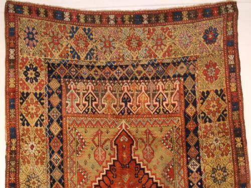 fig 1. An antique mid-19th century Turkish Mujur prayer rug featuring a central terracotta stepped mihrab niche framed by intricate multi-coloured geometric borders.
