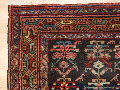 fig 1. A long narrow antique Luri wool runner carpet with repeating colourful geometric tribal motifs on a dark indigo background framed by decorative multi-band borders.