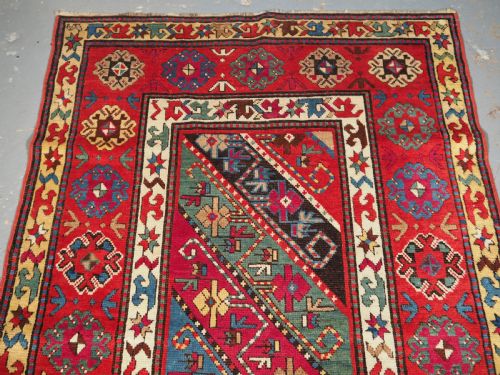fig 1. An antique Caucasian Gendje Kazak hand-knotted wool rug featuring diagonal polychrome stripes within a wide geometric border on a red field.